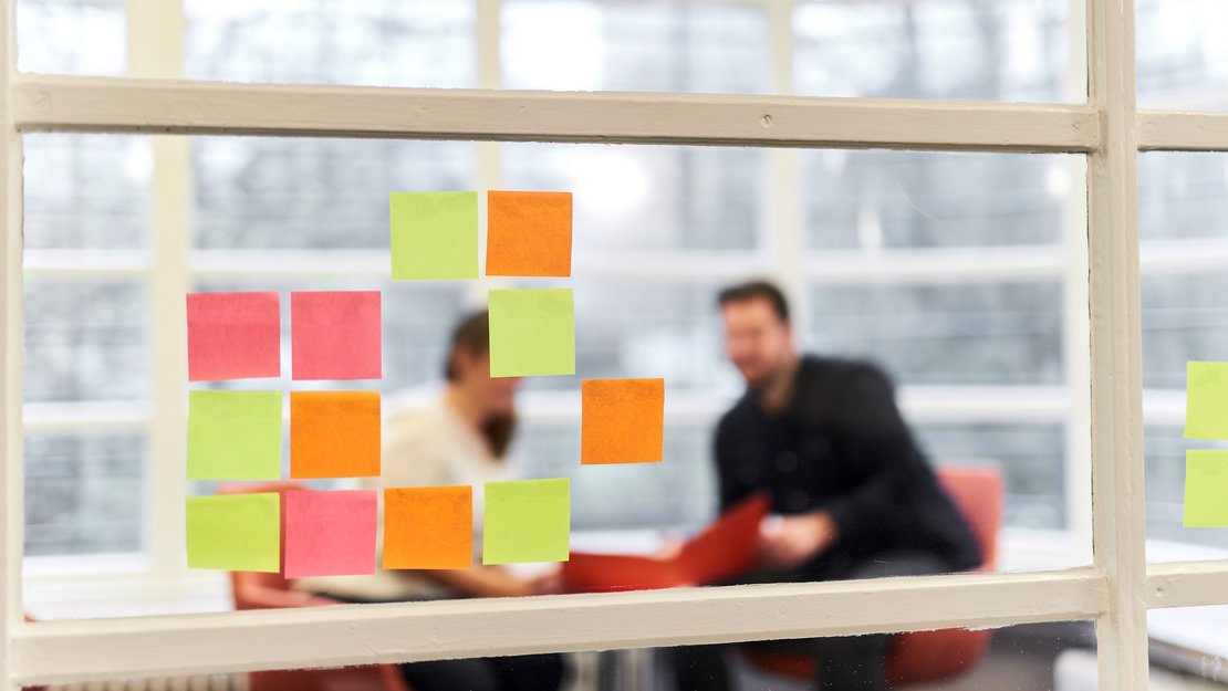 Studierende an einer Wand mit bunten Post-It Zetteln